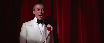 Movie still from “Victor/Victoria” (1982), directed by Blake Edwards – A man in a white suit is singing into a microphone; Close Up shot, Low angle