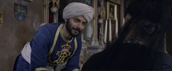 Movie still from “Victoria & Abdul” (2017), directed by Stephen Frears – A man with a turban on in front of a fireplace; Medium shot, Over the shoulder angle