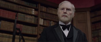 Movie still from “Victoria & Abdul” (2017), directed by Stephen Frears – An old man in a suit and a bow tie in front of a book shelf; Close Up shot, Low angle