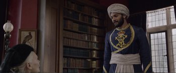 Movie still from “Victoria & Abdul” (2017), directed by Stephen Frears – A man in a turban standing in front of a book shelf; Medium shot, Over the shoulder angle