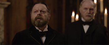 Movie still from “Victoria & Abdul” (2017), directed by Stephen Frears – An old man with a beard and mustache wearing a black suit; Close Up shot, Over the shoulder angle