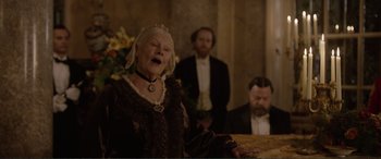 Movie still from “Victoria & Abdul” (2017), directed by Stephen Frears – An older woman is singing in front of two other men; Medium shot, Low angle