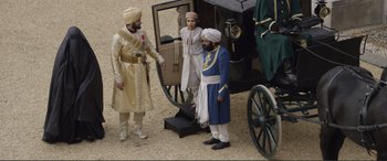 Movie still from “Victoria & Abdul” (2017), directed by Stephen Frears – A group of men standing next to each other near a carriage; Wide shot, High angle