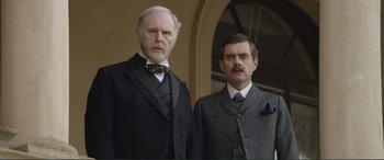 Movie still from “Victoria & Abdul” (2017), directed by Stephen Frears – Two men in suits and ties standing next to each other; Medium shot, Low angle