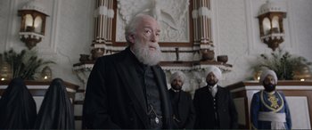 Movie still from “Victoria & Abdul” (2017), directed by Stephen Frears – A man with a long white beard standing in front of two other men; Medium shot, Low angle