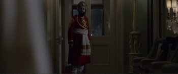 Movie still from “Victoria & Abdul” (2017), directed by Stephen Frears – A man dressed in a red and white outfit standing in front of a door; Medium shot, Over the shoulder angle