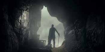 Movie still from “House of the Dragon” (2022), created by George R.R. Martin – A man standing inside of a cave holding a sword; Wide shot, Low angle