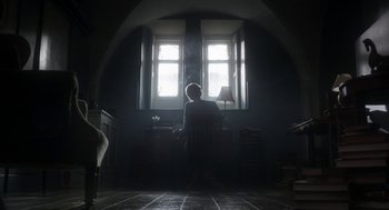 Movie still from “Vita & Virginia” (2018), directed by Chanya Button – A person sitting at a desk in front of a window; Wide shot, Low angle