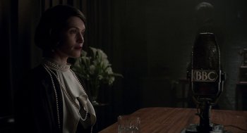 Movie still from “Vita & Virginia” (2018), directed by Chanya Button – A woman sitting at a wooden table in a dark room; Medium shot, Over the shoulder angle