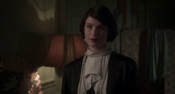 Movie still from “Vita & Virginia” (2018), directed by Chanya Button – A woman in a black jacket and pearls standing next to a lamp; Close Up shot, Low angle