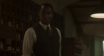 Movie still from “Vita & Virginia” (2018), directed by Chanya Button – A man wearing a suit and tie standing in a dark room; Medium shot, Over the shoulder angle