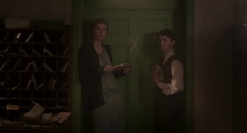 Movie still from “Vita & Virginia” (2018), directed by Chanya Button – A woman and a man standing next to each other in front of a green door; Medium shot, Low angle