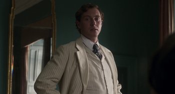 Movie still from “Vita & Virginia” (2018), directed by Chanya Button – A man in a suit and tie standing in front of a mirror; Medium shot, Low angle