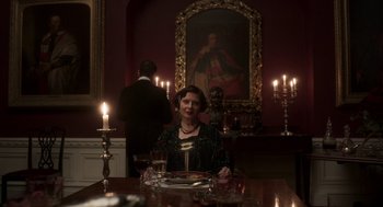 Movie still from “Vita & Virginia” (2018), directed by Chanya Button – A woman sitting at a dinner table in front of a painting; Medium shot, Low angle