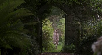 Movie still from “Vita & Virginia” (2018), directed by Chanya Button – A woman standing in the middle of an archway in a garden; Extreme Wide shot, Over the shoulder angle