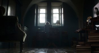 Movie still from “Vita & Virginia” (2018), directed by Chanya Button – A woman sitting at a desk in front of an open window; Wide shot, Low angle