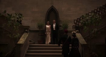 Movie still from “Vita & Virginia” (2018), directed by Chanya Button – A man and a woman standing in front of an archway; Wide shot, High angle