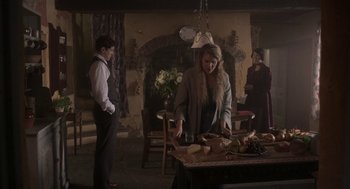 Movie still from “Vita & Virginia” (2018), directed by Chanya Button – A woman standing at a table cutting up food; Wide shot, Over the shoulder angle