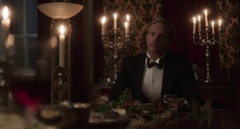 Movie still from “Vita & Virginia” (2018), directed by Chanya Button – A man sitting at a dinner table in front of candles; Medium shot, Over the shoulder angle