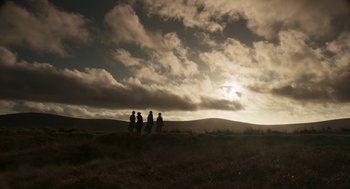 Movie still from “Vita & Virginia” (2018), directed by Chanya Button – A group of people standing on top of a grass covered field; Extreme Wide shot, Low angle