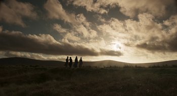 Movie still from “Vita & Virginia” (2018), directed by Chanya Button – A group of people standing on top of a grass covered field; Extreme Wide shot, Low angle