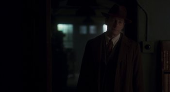 Movie still from “Vita & Virginia” (2018), directed by Chanya Button – A man wearing a suit and a hat standing in a dark room; Medium shot, Over the shoulder angle
