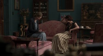 Movie still from “Vita & Virginia” (2018), directed by Chanya Button – Two women are sitting on a pink couch in a living room; Medium shot, Over the shoulder angle