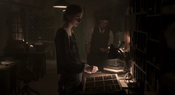 Movie still from “Vita & Virginia” (2018), directed by Chanya Button – A woman standing in front of a table with a box; Medium shot, Over the shoulder angle