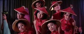 Movie still from “Viva Las Vegas” (1964), directed by George Sidney – A group of asian women in red dresses and hats; Medium shot, Low angle