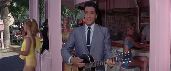 Movie still from “Viva Las Vegas” (1964), directed by George Sidney – A man in a suit and tie holding a guitar; Medium shot, Over the shoulder angle