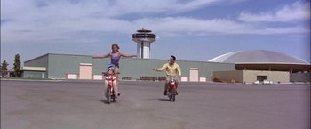 Movie still from “Viva Las Vegas” (1964), directed by George Sidney – A man and a woman riding bikes in a parking lot; Wide shot, Low angle