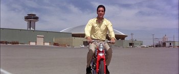 Movie still from “Viva Las Vegas” (1964), directed by George Sidney – A man is riding a bike in a parking lot; Extreme Wide shot, Low angle