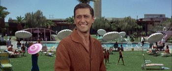 Movie still from “Viva Las Vegas” (1964), directed by George Sidney – A man smiling for a picture while standing next to a swimming pool; Medium shot, Low angle