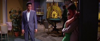 Movie still from “Viva Las Vegas” (1964), directed by George Sidney – A group of people standing in a room with a wheel of fortune on the wall; Medium shot, Over the shoulder angle