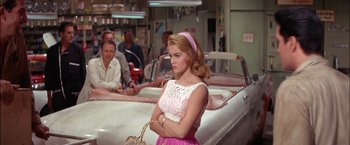 Movie still from “Viva Las Vegas” (1964), directed by George Sidney – A woman in a white and pink dress holding a purse; Medium shot, Over the shoulder angle