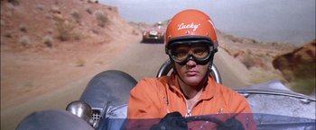 Movie still from “Viva Las Vegas” (1964), directed by George Sidney – A person in an orange racing suit driving a race car; Close Up shot, Low angle