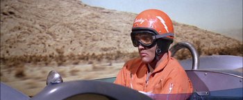 Movie still from “Viva Las Vegas” (1964), directed by George Sidney – A man in an orange racing suit sitting in a car; Medium shot, Low angle
