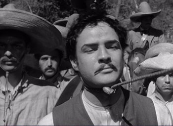 Movie still from “Viva Zapata!” (1952), directed by Elia Kazan – Black and white photograph of a man smoking a pipe in front of other men; Close Up shot, Low angle