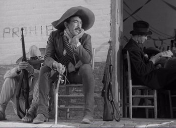 Movie still from “Viva Zapata!” (1952), directed by Elia Kazan – A man sitting on top of a chair wearing a cowboy hat; Medium shot, Low angle