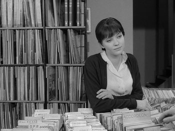 Movie still from “My Life to Live” (1962), directed by Jean-Luc Godard – A woman sitting in front of a table full of records; Medium shot, High angle