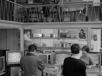 Movie still from “My Life to Live” (1962), directed by Jean-Luc Godard – A black and white photo of people looking at televisions; Wide shot, High angle