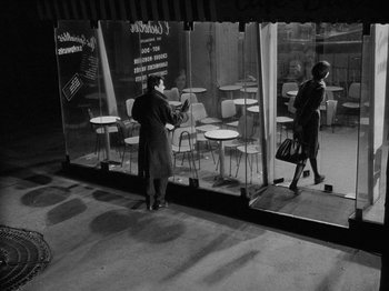 Movie still from “My Life to Live” (1962), directed by Jean-Luc Godard – A man and a woman are standing in front of a store; Wide shot, High angle