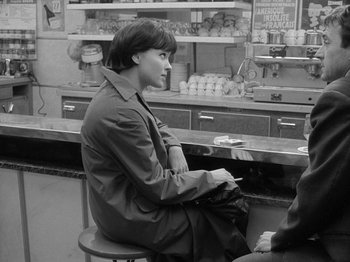 Movie still from “My Life to Live” (1962), directed by Jean-Luc Godard – A man sitting at a counter in a restaurant; Medium shot, Over the shoulder angle