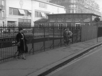 Movie still from “My Life to Live” (1962), directed by Jean-Luc Godard – A black - and - white photo of people walking on a sidewalk; Extreme Wide shot, High angle