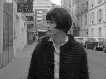 Movie still from “My Life to Live” (1962), directed by Jean-Luc Godard – A young woman standing on the side of a street; Medium shot, High angle