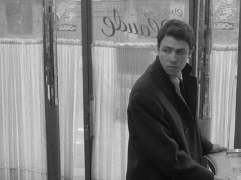 Movie still from “My Life to Live” (1962), directed by Jean-Luc Godard – A black and white photo of a man standing in front of a window; Medium shot, Low angle