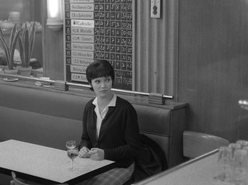 Movie still from “My Life to Live” (1962), directed by Jean-Luc Godard – A woman sitting at a table with a glass of wine; Medium shot, Over the shoulder angle