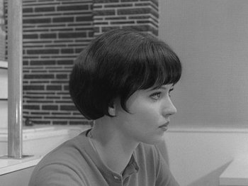 Movie still from “My Life to Live” (1962), directed by Jean-Luc Godard – A woman with short hair sitting in front of a brick wall; Close Up shot, Over the shoulder angle