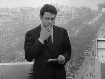 Movie still from “My Life to Live” (1962), directed by Jean-Luc Godard – A black and white photo of a man smoking a cigarette; Medium shot, High angle