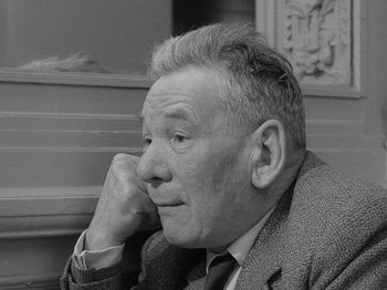 Movie still from “My Life to Live” (1962), directed by Jean-Luc Godard – An older man sitting in front of a wall with his hand under his chin; Close Up shot, Low angle